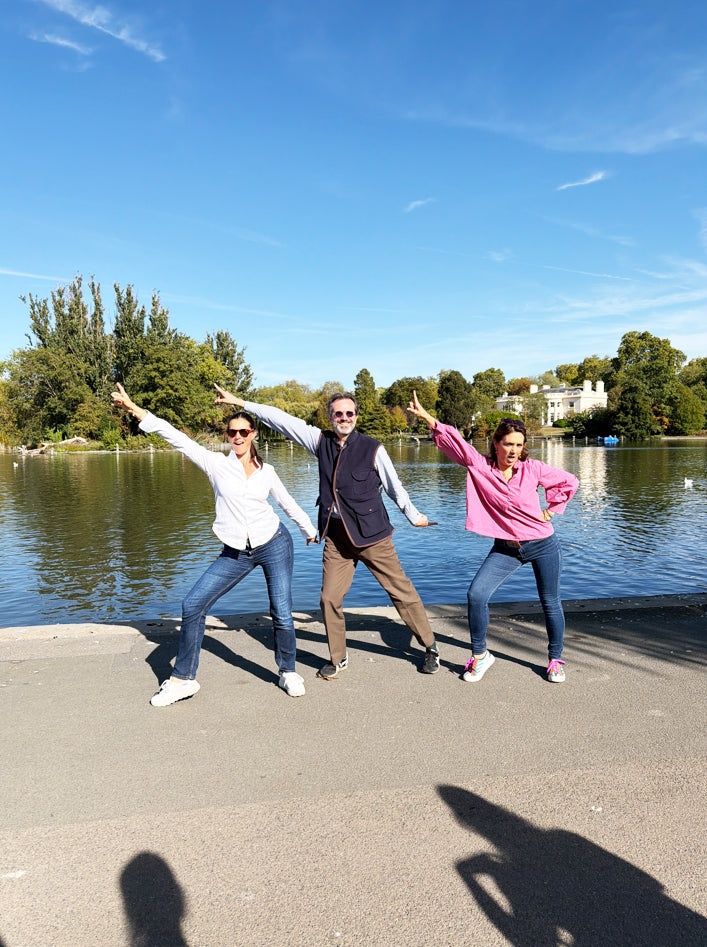 Three friends posing with arms outstretched beside a lake in a park on a sunny treasure hunt