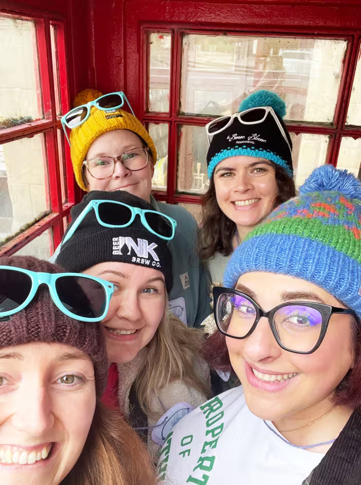 Group of friends in beanies and sunglasses squeezed into a red phone box for a treasure hunt selfie