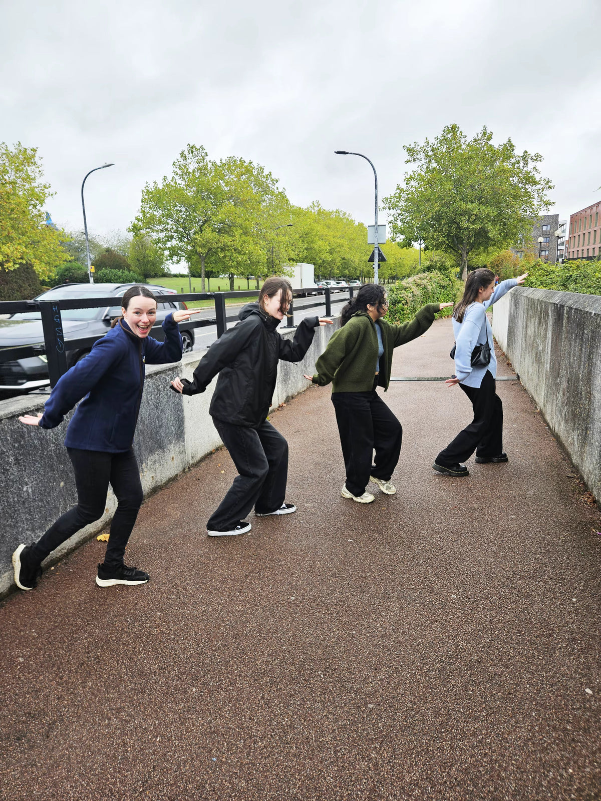 Four friends doing a silly walk in a line along a path for a scavenger hunt photo challenge
