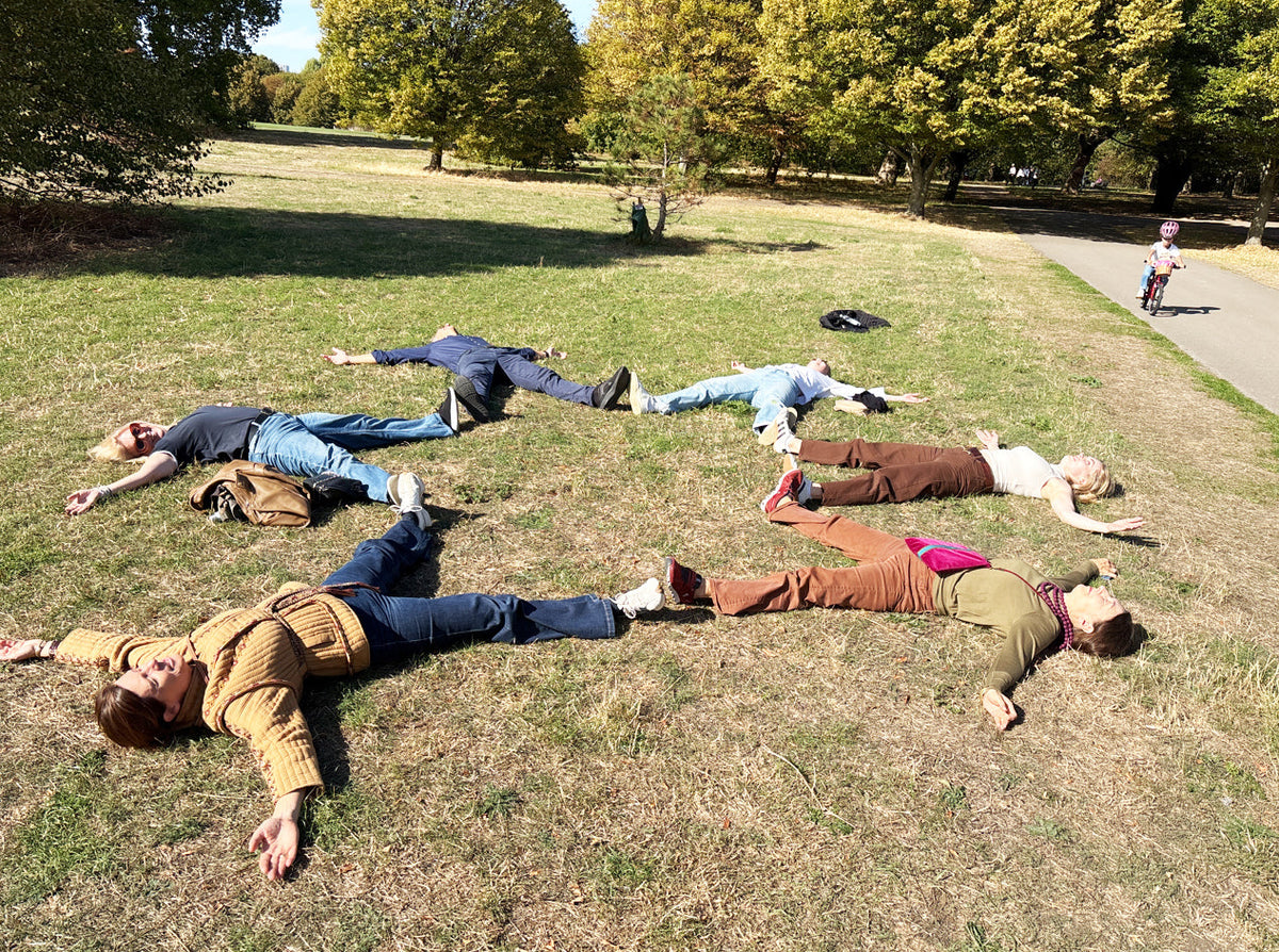 Group of friends lying on the grass in a star shape in a park for a treasure hunt photo challenge