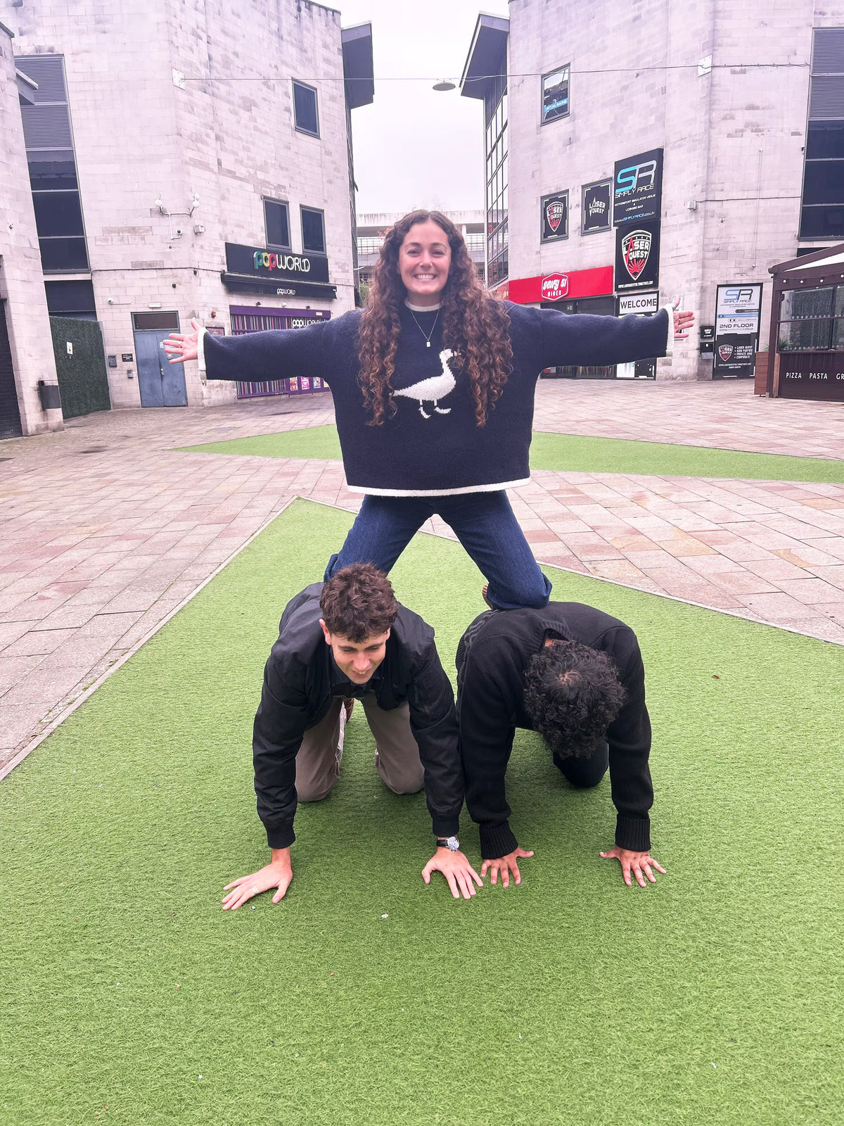 Friends building a human pyramid in a city square for a party scavenger hunt photo challenge