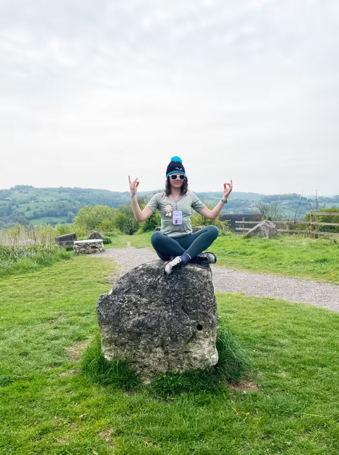 Woman in a beanie striking a meditation pose on a rock overlooking the countryside during a treasure hunt