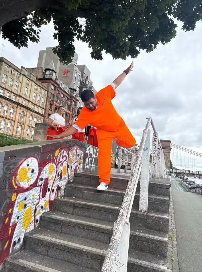 Man in an orange jumpsuit striking a pose on graffiti-covered riverside steps during a city treasure hunt