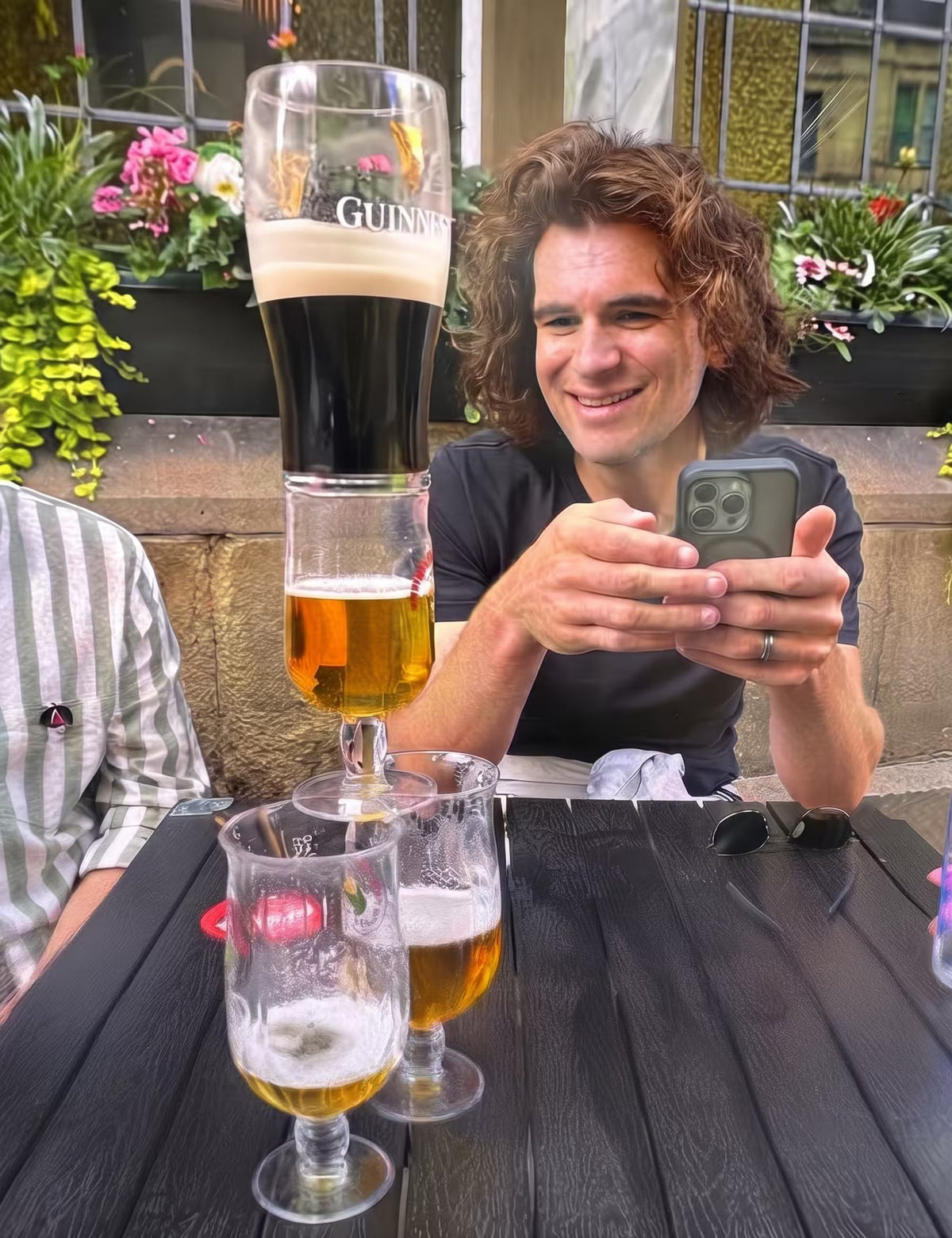 Man smiling at his phone after balancing a pint of Guinness on stacked glasses for a treasure hunt pub challenge
