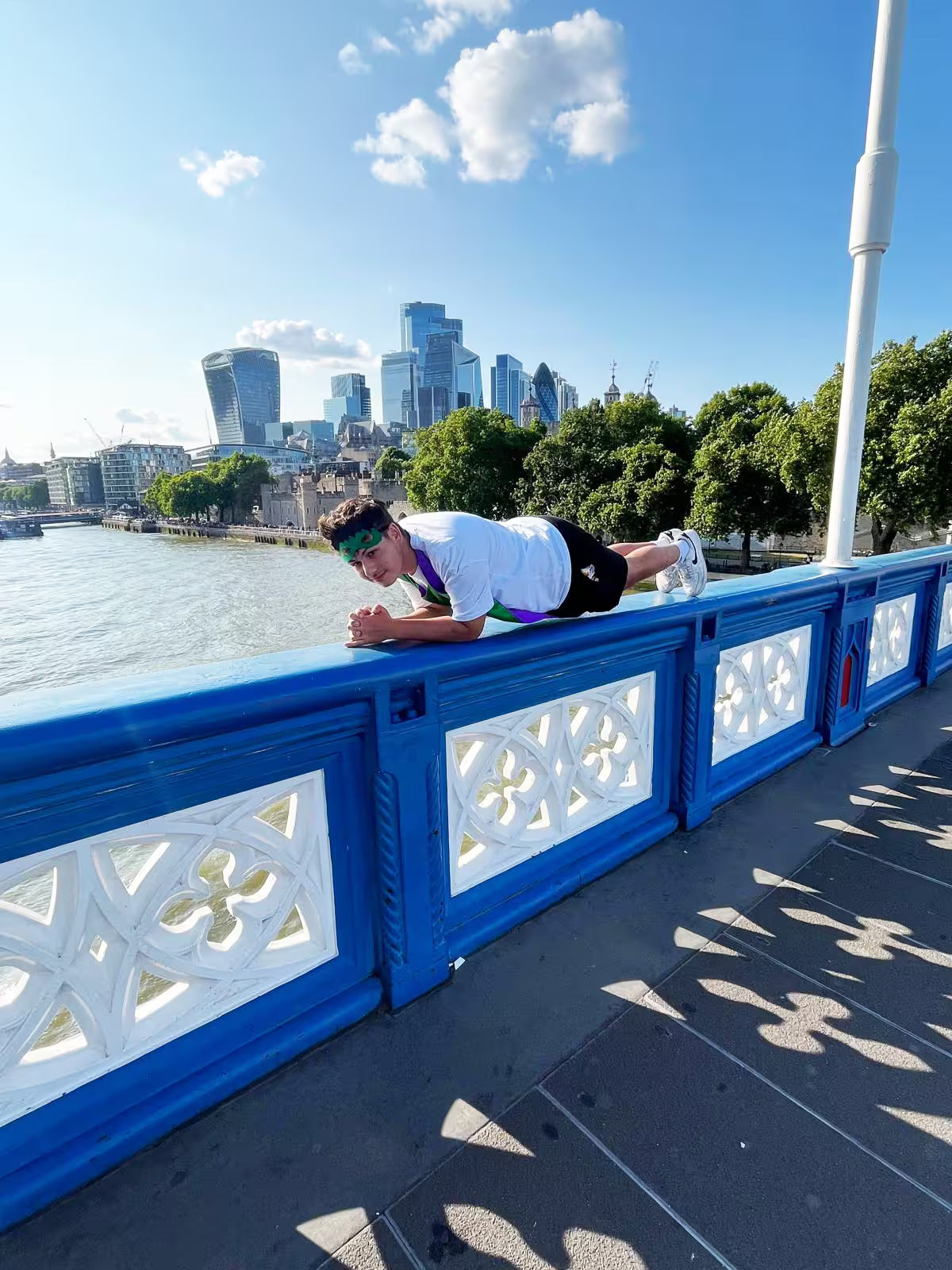 Man planking on the railings of Tower Bridge with the City of London skyline behind during a London treasure hunt photo challenge