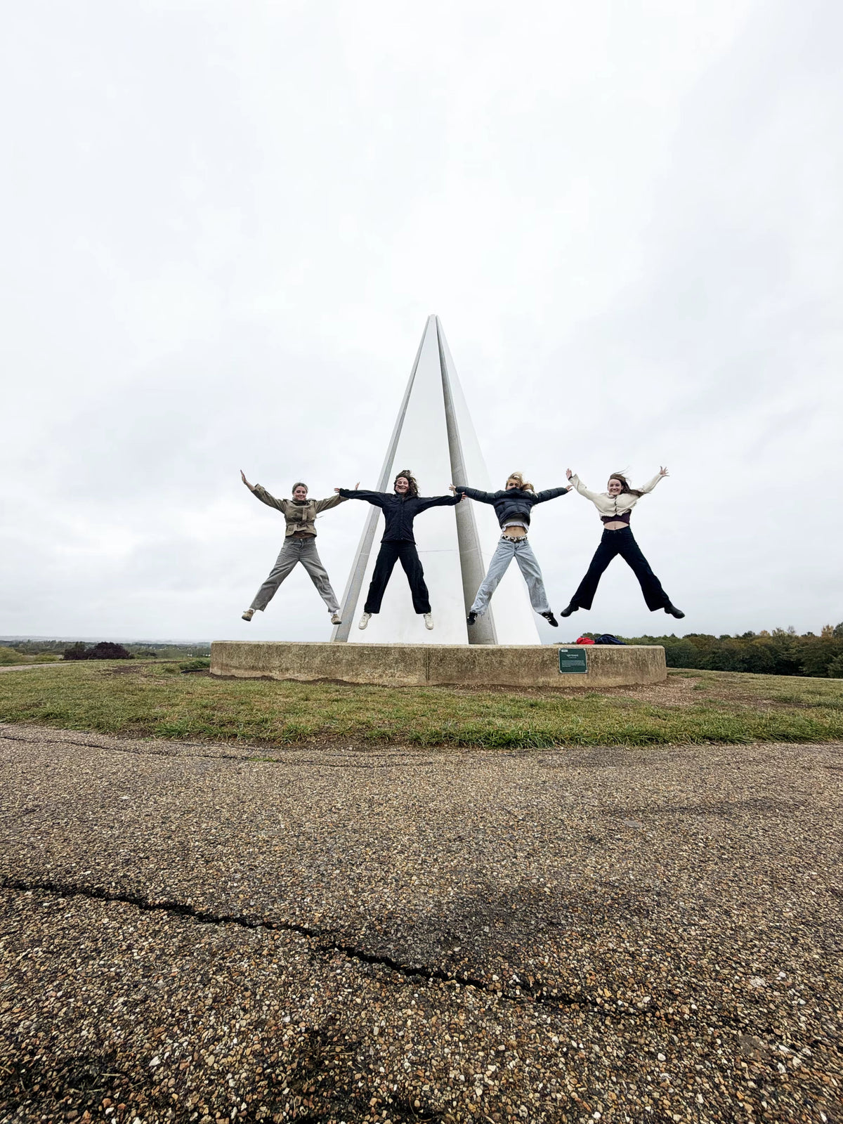 Four friends doing star jumps in front of a white hilltop monument on a treasure hunt
